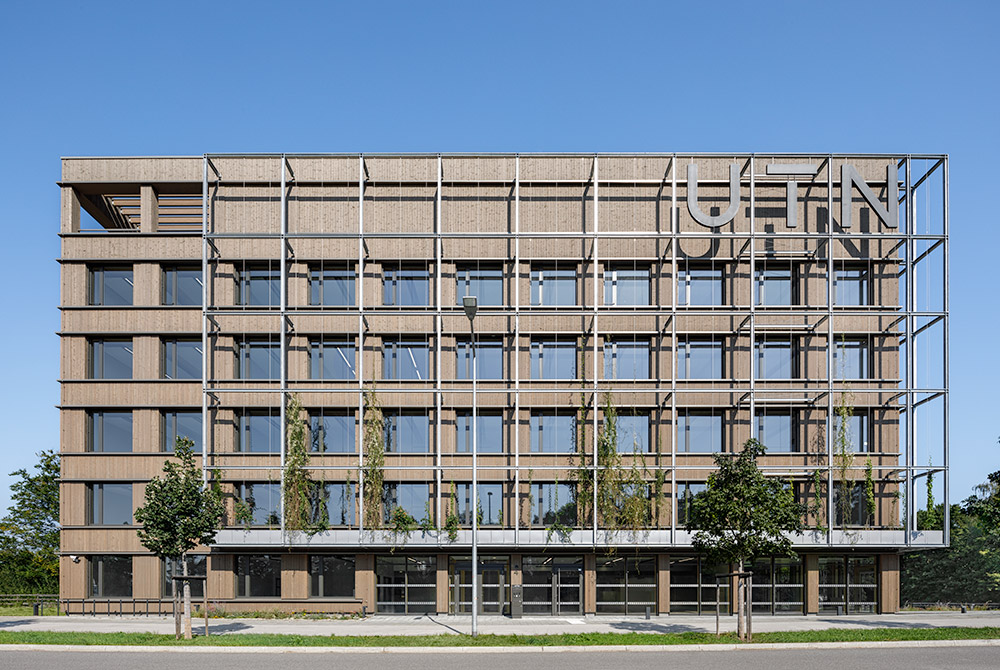 Cube One in Frontalansicht. Erstes Gebäude der Technischen Universität auf dem Campus, gebaut in Holzbauweise mit vielen Fenstern, Flachdach und Rankgerüst