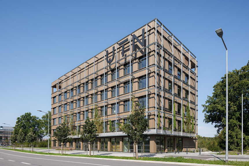 Cube One in Seitenansicht von links. Erstes Gebäude der Technischen Universität auf dem Campus, gebaut in Holzbauweise mit vielen Fenstern, Flachdach und Rankgerüst